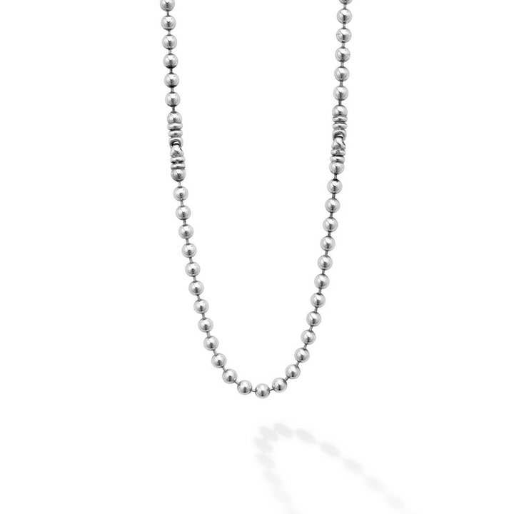 A close-up of a white gold beaded necklace with beaded stations against a white background.