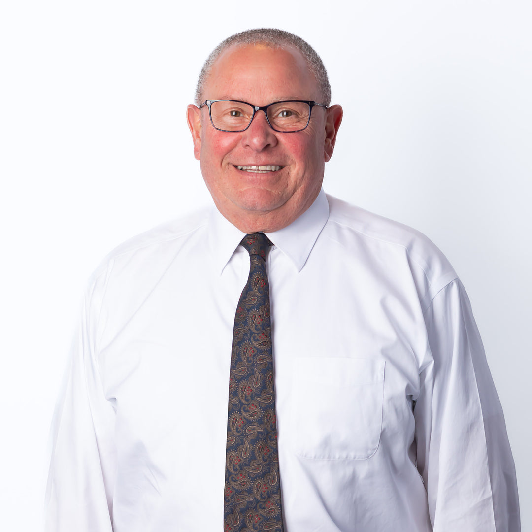 A headshot of a man smiling with short hair and glasses wearing a button-down and a paisley tie.