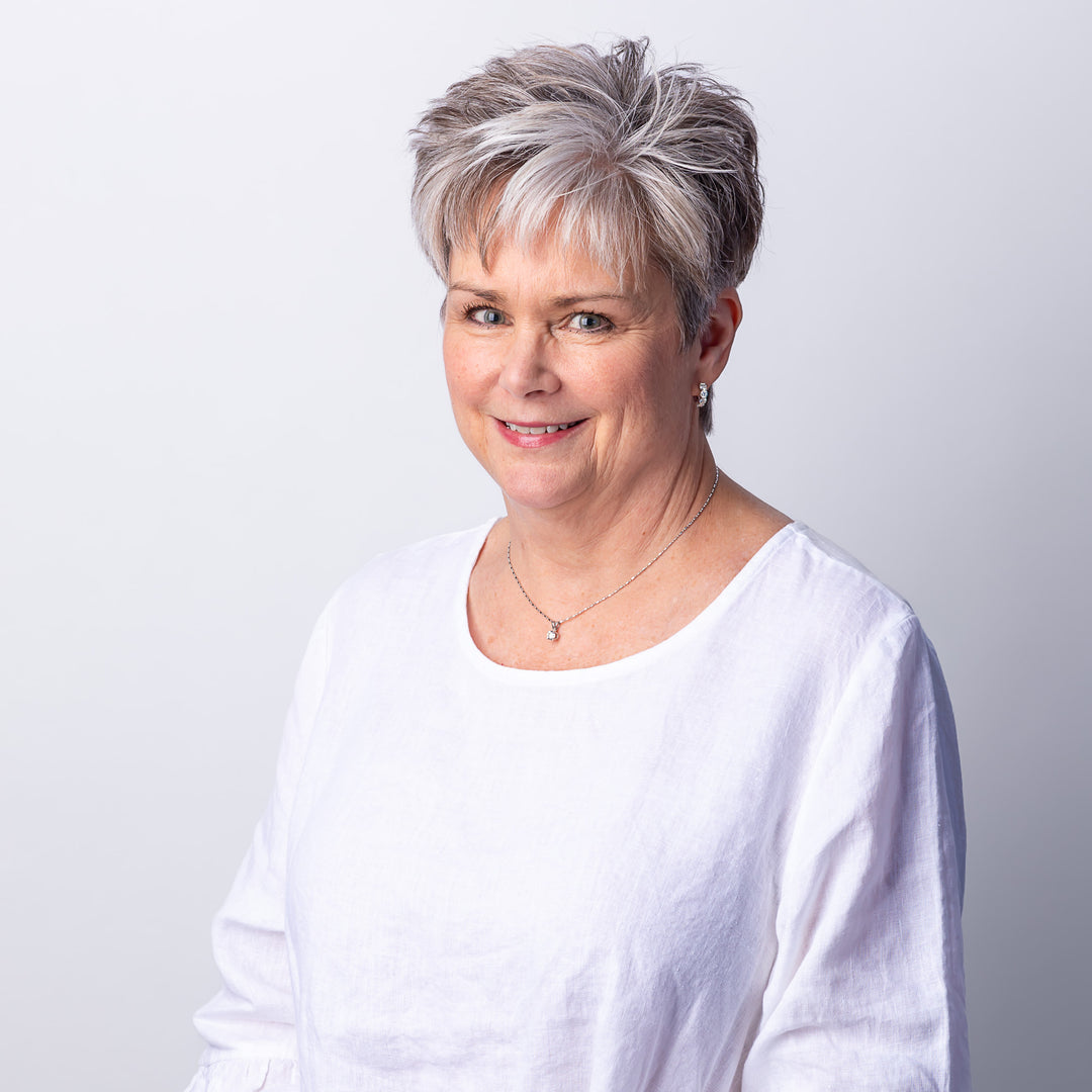 A headshot of a woman with short hair smiling, wearing a white blouse, silver necklace, and silver earrings.
