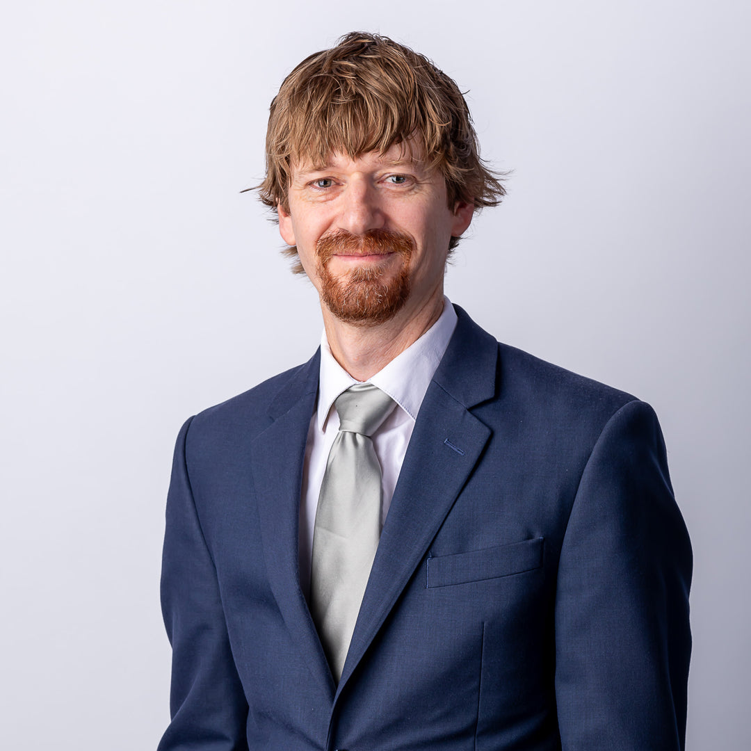 A headshot of a man with short hair and facial hair smiling, wearing a suit and tie.