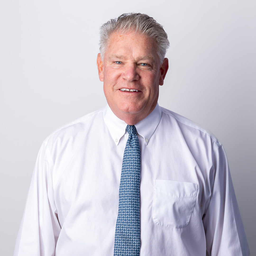 A head-shot of a man smiling and wearing a white button-down and blue-patterned design.