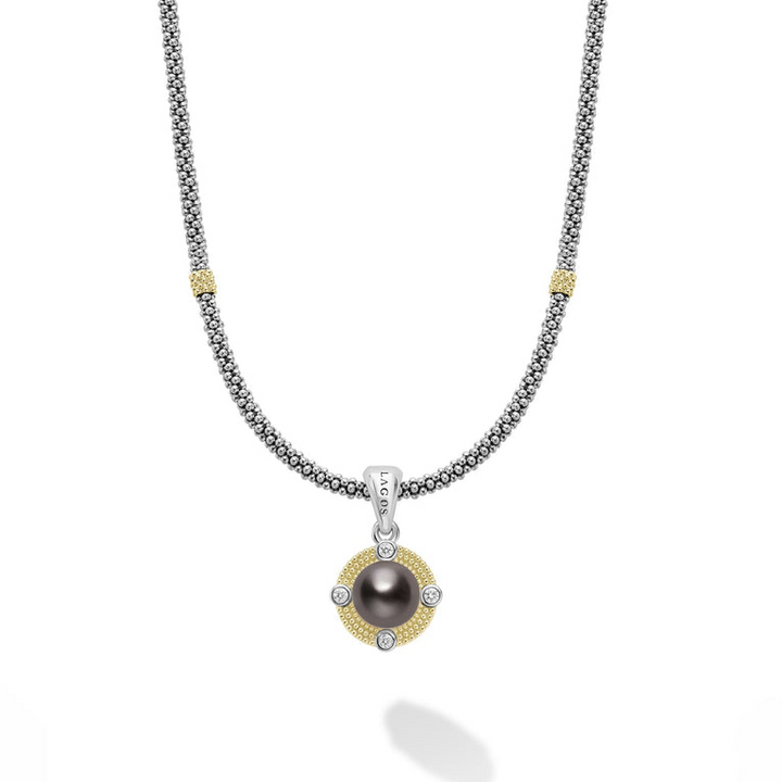 A white gold necklace is in the middle of a white background. The bracelet features a black pearl center stone and a yellow-gold caviar beaded halo pendant, a LAGOS engraved loop, and a caviar beaded chain with yellow-gold stations.