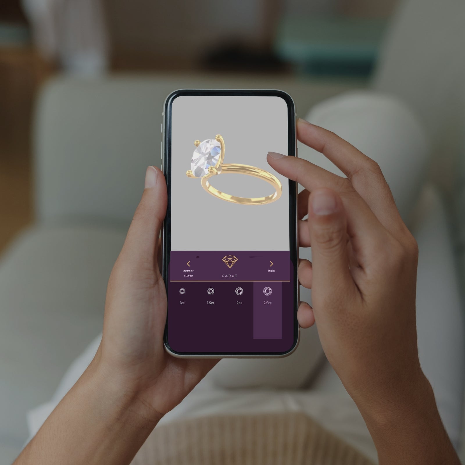 A close-up of a person holding their iPhone up with both hands. The iPhone features the Richter and Phillips 3D Ring Designer with a Yellow Gold ring displayed in the middle with an oval-shaped diamond. A purple menu option at the bottom shows the different carat sizes.