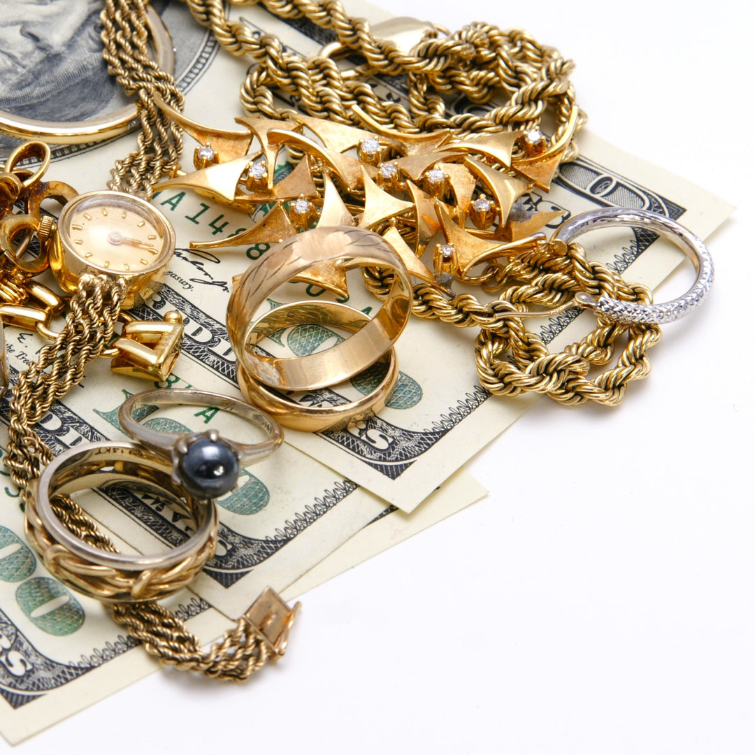 photo of gold necklaces, gold brooches, gold bracelets, gold watches, silver earrings, silver rings sitting in a pile on top of 100 dollar bills