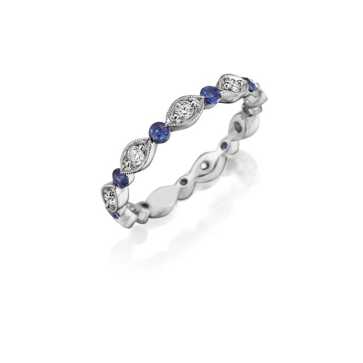 An angled view of a white gold wedding band against a white background. The ring features an alternating prong-set round diamonds, surrounded by intricate marquise detailing, and a sapphire round center stone.