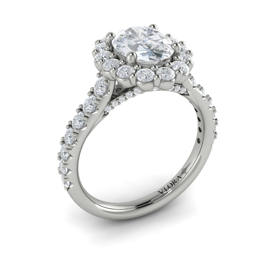 An angled view of a white gold engagement ring is set against a white background. The engagement ring features an oval center diamond, a cathedral setting, a diamond-set halo, and a diamond-set band.