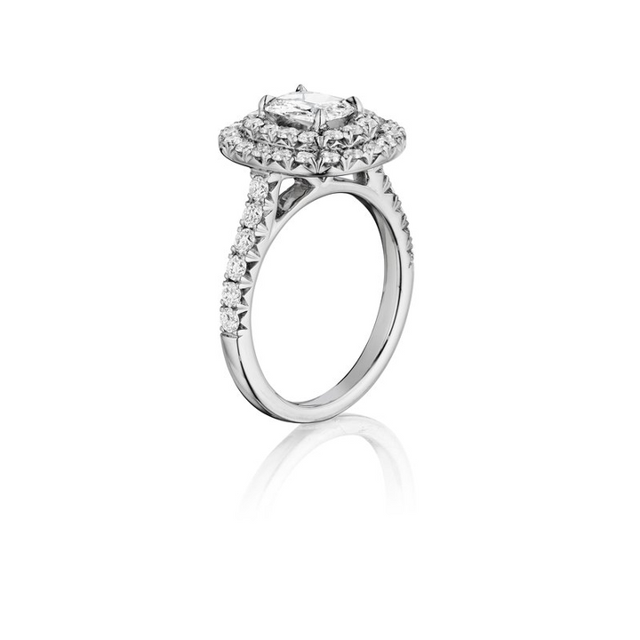 This is an angled view of a white gold ring against a white background. The ring features a brilliant center stone embraced by two dazzling halos of diamonds.