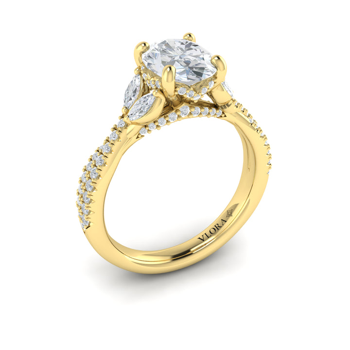 An angled view of a yellow gold engagement ring is set against a white background. The engagement ring features a vine-inspired band of intertwining pavé diamonds. Two marquise diamonds rest like leaves, embracing the oval center diamond in a Vlora signature V-shaped setting with a hidden halo and pave details.