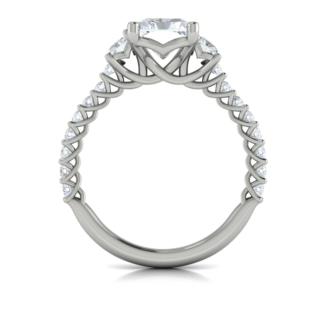 A top view of a white gold engagement ring is set against a white background. The engagement ring features a center emerald cut diamond flanked by two emerald cut side diamonds, an intricate woven setting, and a diamond-set band.