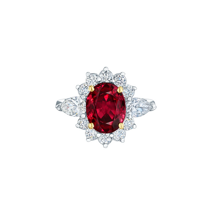 A white gold ring is in the middle of a white background. The ring features an oval-shaped ruby center stone set with yellow gold prongs with round and marquise-shaped side stone diamonds.
