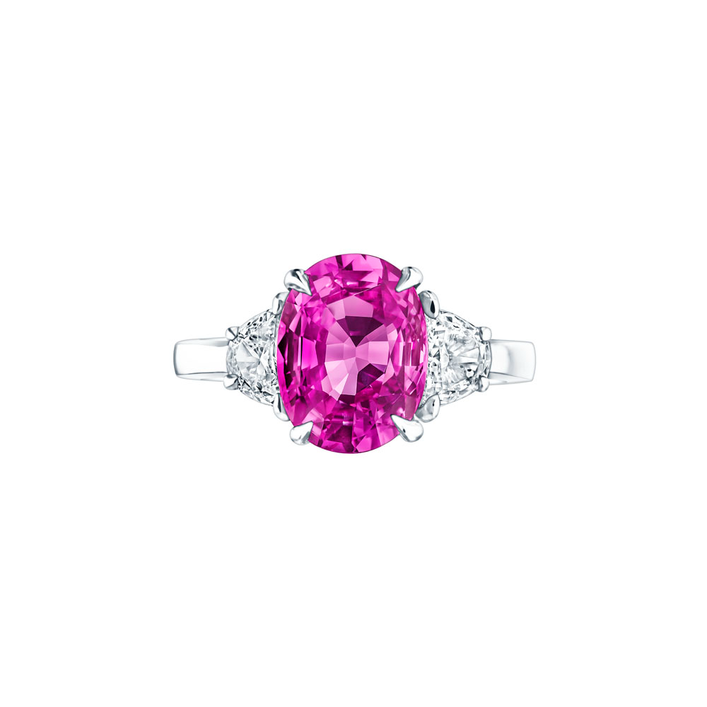 A front view of a white gold diamond ring against a white background. The ring features a 3-stone design with an oval-cut pink sapphire at the center, framed by two perfectly matched half-moon diamond side stones.