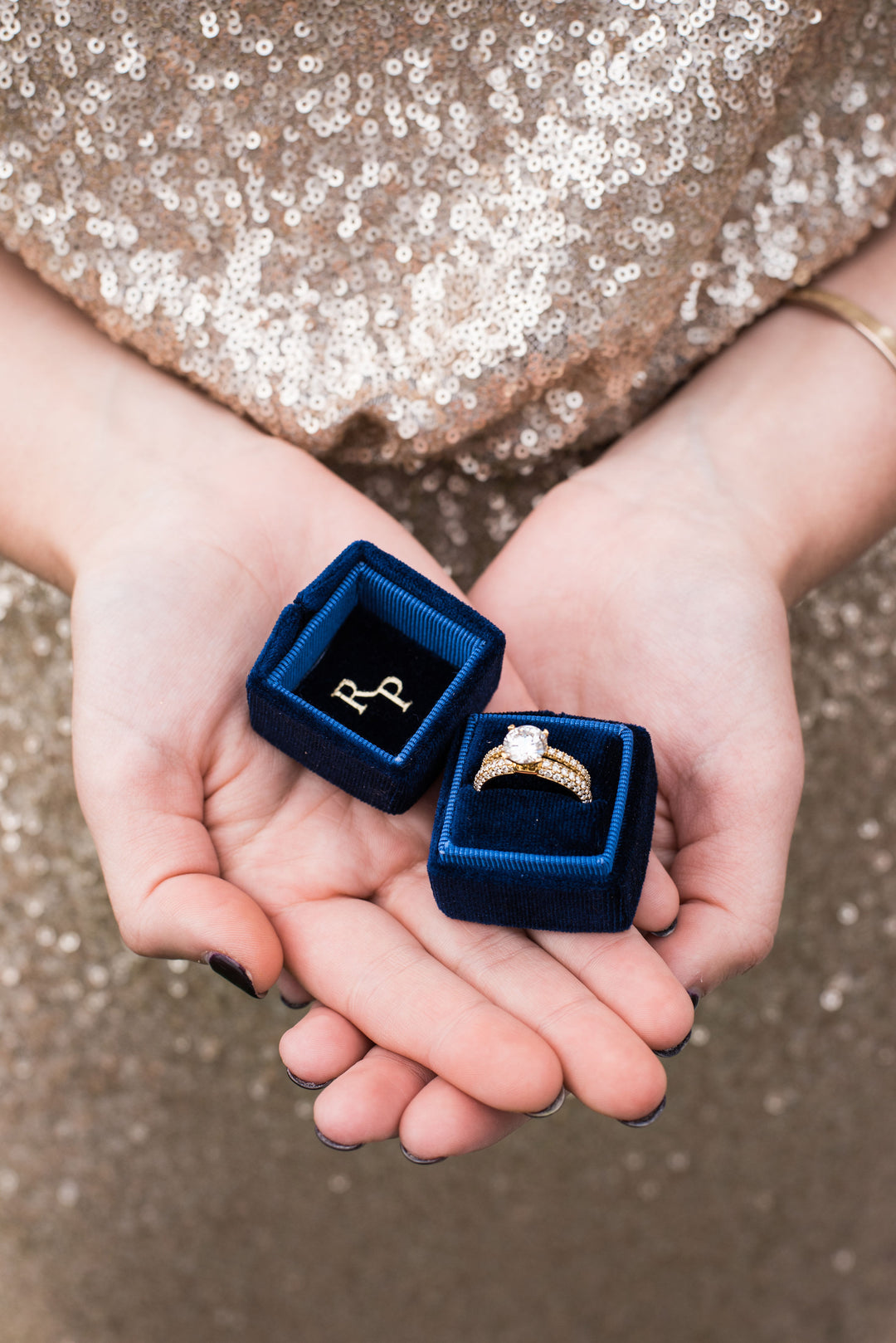 photo of a woman in a gold sequin dress holding a blue Richter & Phillips ring box - with a diamond engagement ring and diamond wedding band - in the palms of both her hands