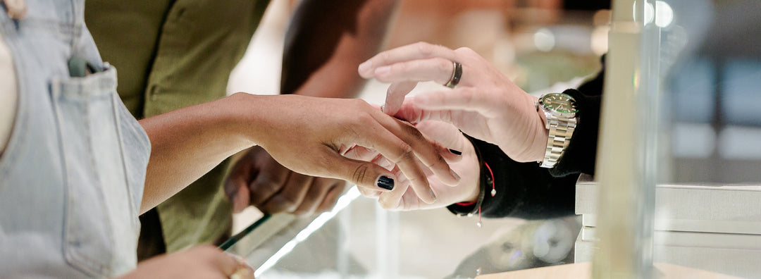 photo of a woman holding her hand out while another person puts a diamond engagement ring on her left hand's ring finger