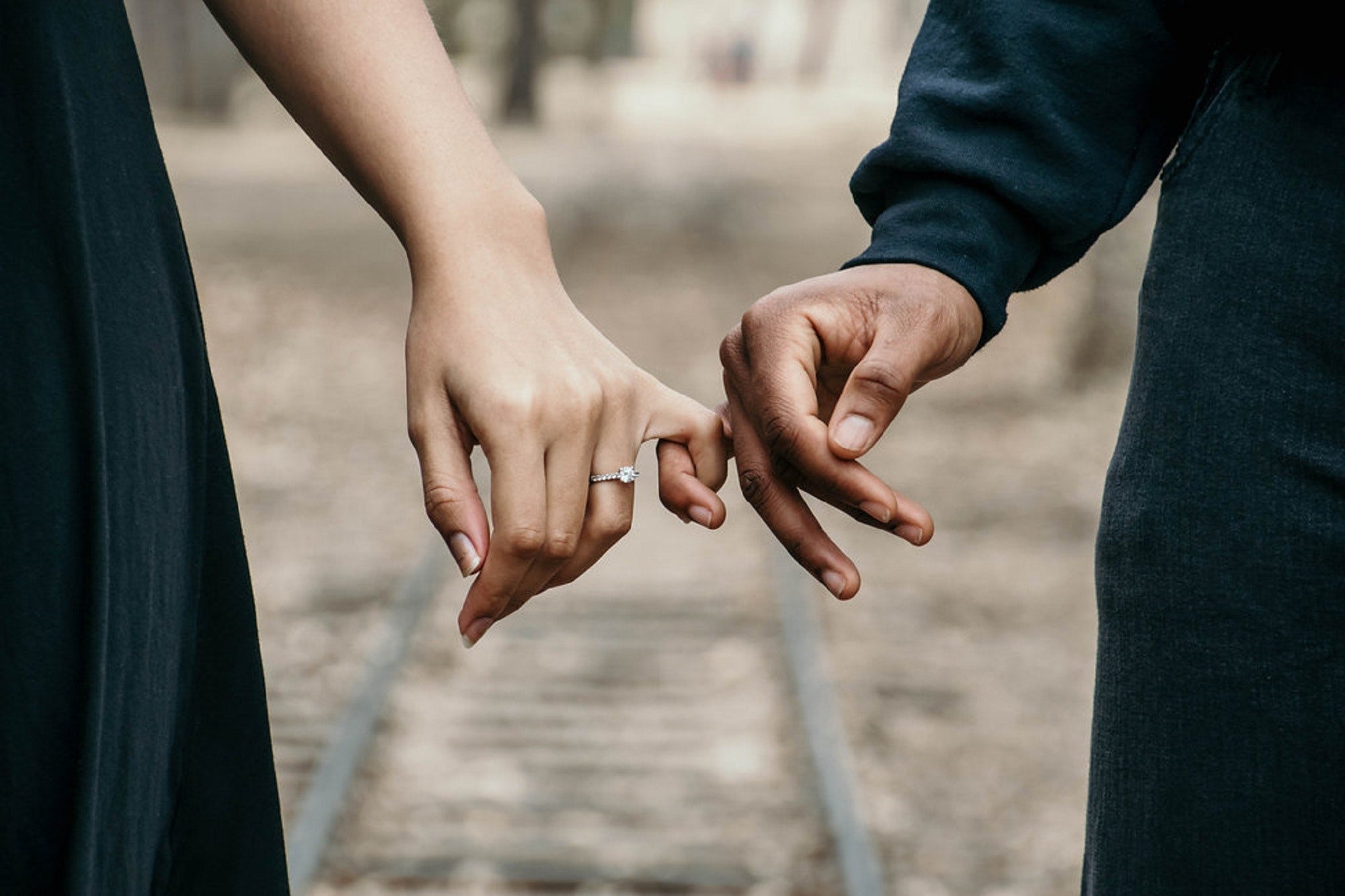 This is a photo of a man and woman locking their pinky fingers, showcasing the engagement ring on the woman's finger.