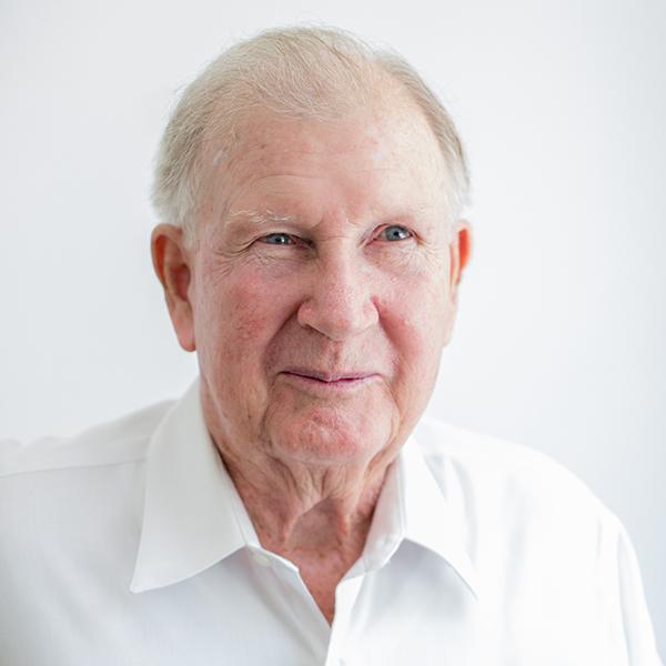 A headshot of a man smiling, wearing a white button down, against a white background.