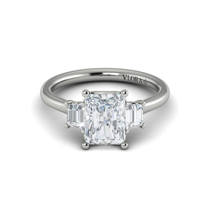A front view of a white gold engagement ring is set against a white background. The engagement ring features an emerald cut center diamond, flanked by complementary emerald cut side stones, in a woven setting.