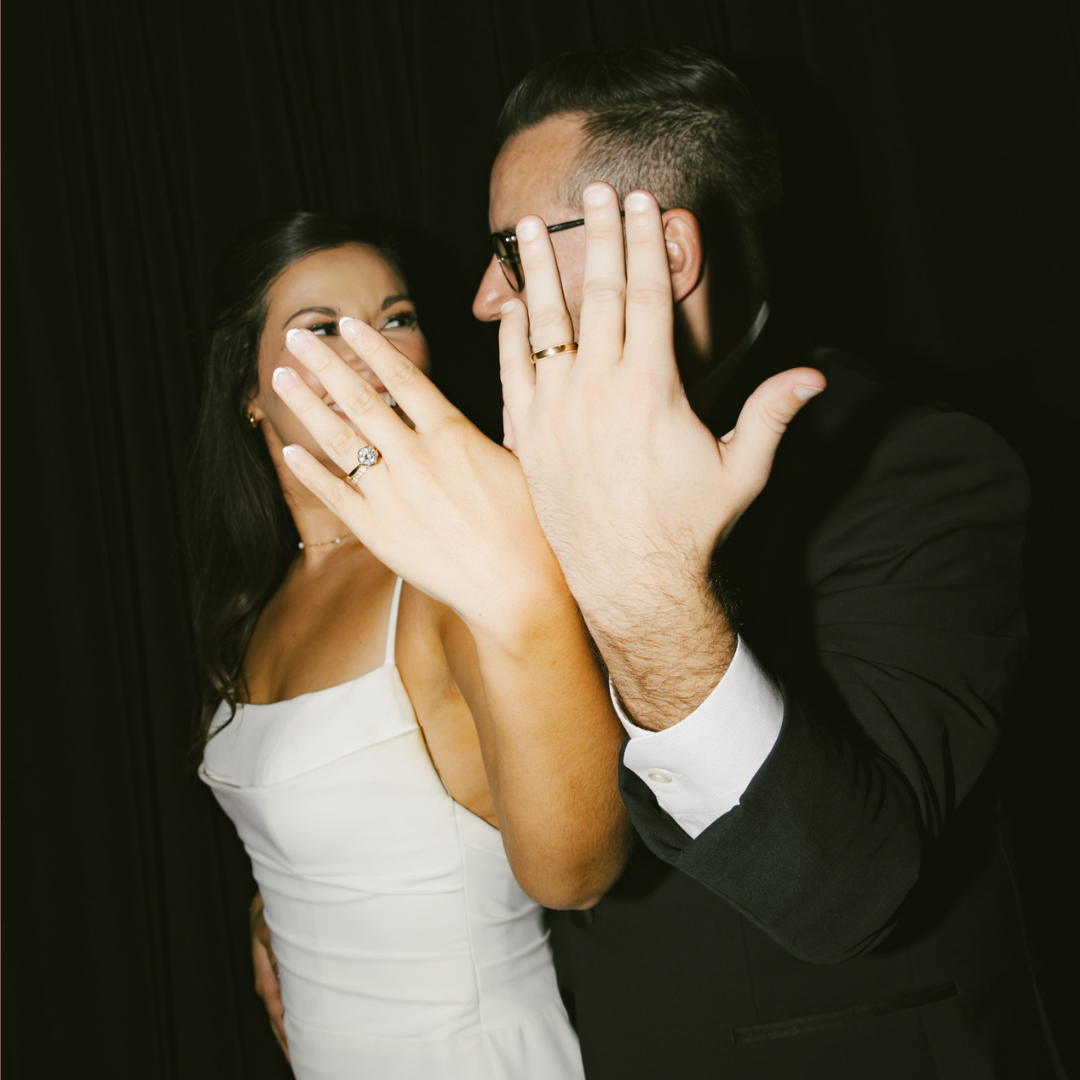 A picture of a bride and groom holding out their hands to show their rings.