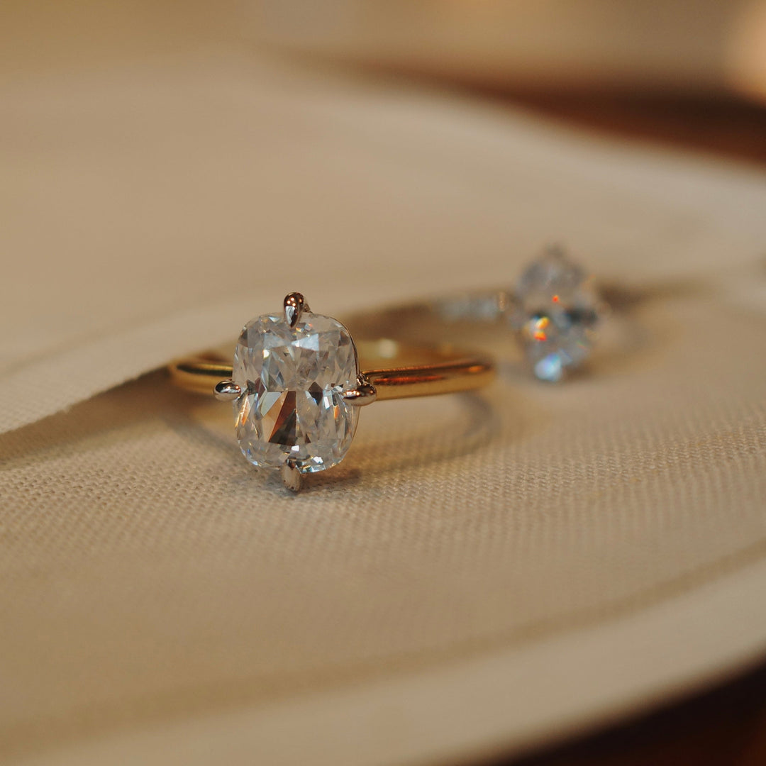 A close-up of two engagement rings with compass prong settings on a yellow cloth.