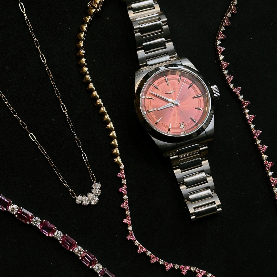 A close-up of various jewelry and a watch with a pink dial