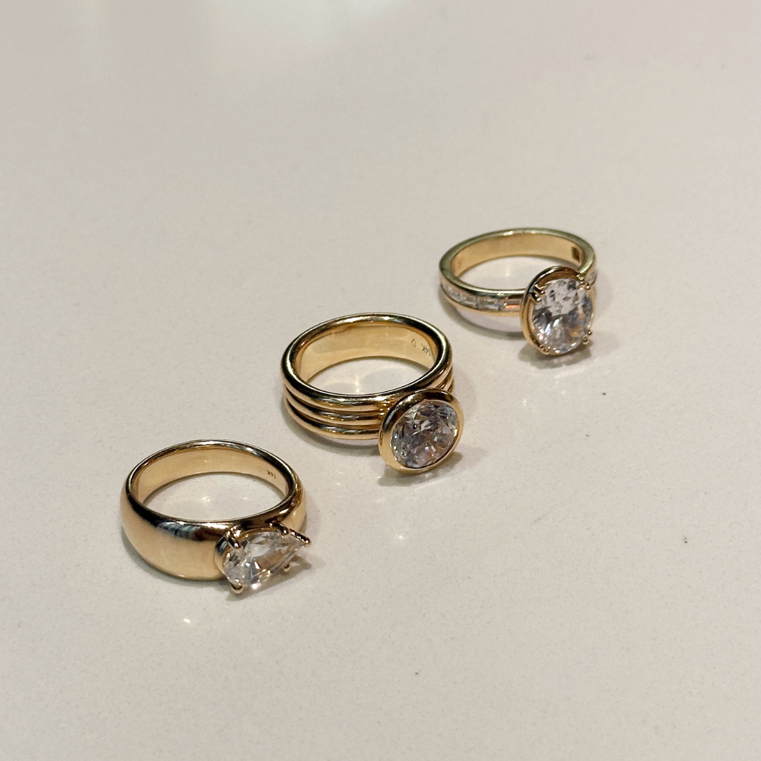 A close up of three different gold engagement rings with different diamonds and settings.