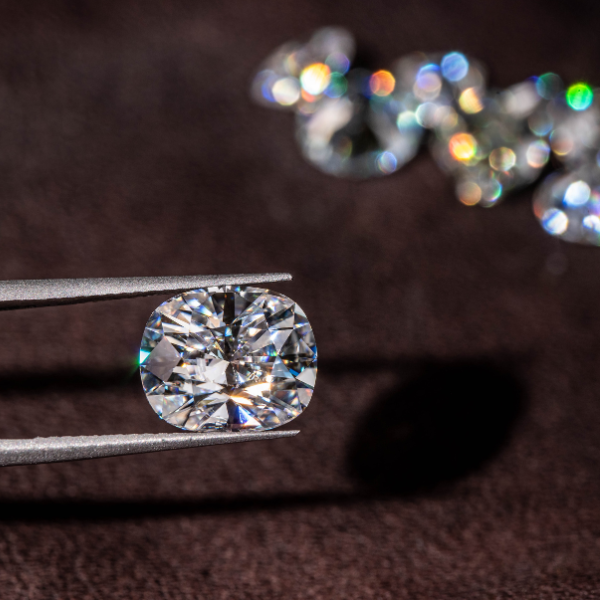close up photo of a diamond being held between the prongs of tweezers with several out of focus diamonds in the background