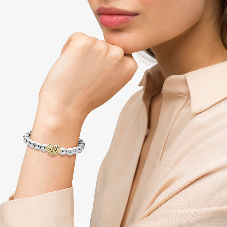 A woman is wearing a sterling silver and 18k gold beaded bracelet featuring an 18k gold and silver Caviar beaded heart accent