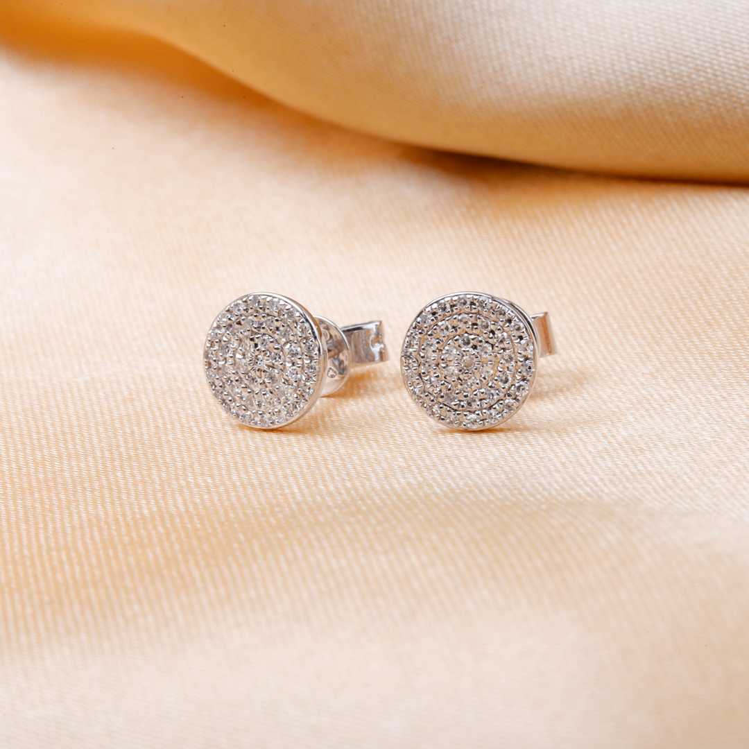 A pair of stud earrings with round, brilliant cut diamonds framed in a pave setting resting against a gold background.