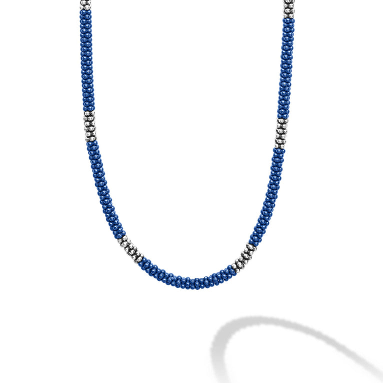 A close-up of a sterling silver and ceramic beaded necklace in the middle of a white background featuring blue ceramic and silver Caviar beading.