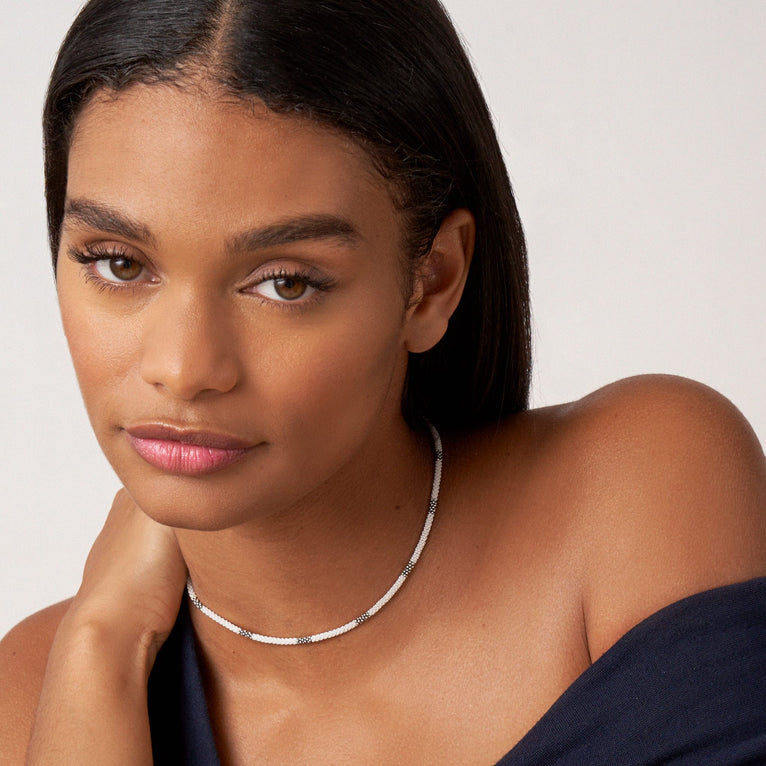 A woman wearing a sterling silver and ceramic beaded necklace featuring white ceramic and silver Caviar beading.