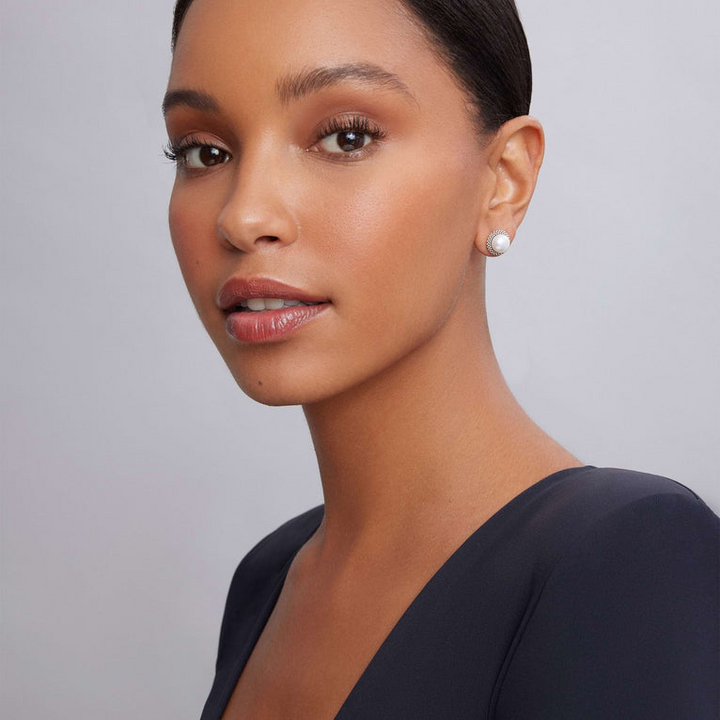 A woman wearing a black top and a pair of classic pearl stud earrings set in signature sterling silver Caviar beading.