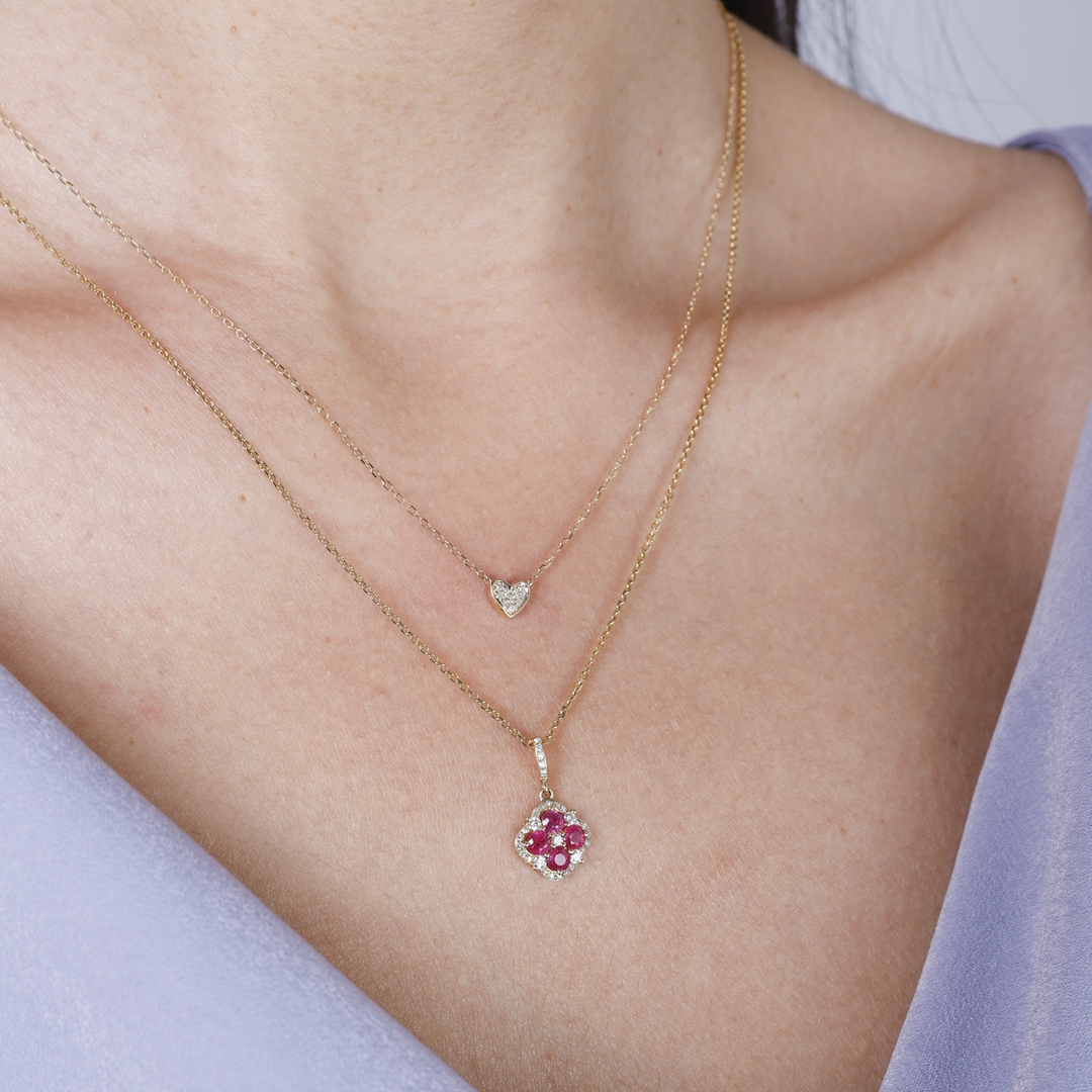 A woman is wearing a yellow-gold Halo Clover Necklace and a purple top. The necklace features a clover motif pendant with ruby round diamonds, milgrain detailing, and a 14k yellow gold chain.