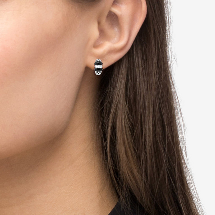 A close-up of a woman wearing a pair of huggie earrings with smooth black ceramic and diamonds with Caviar beading. 