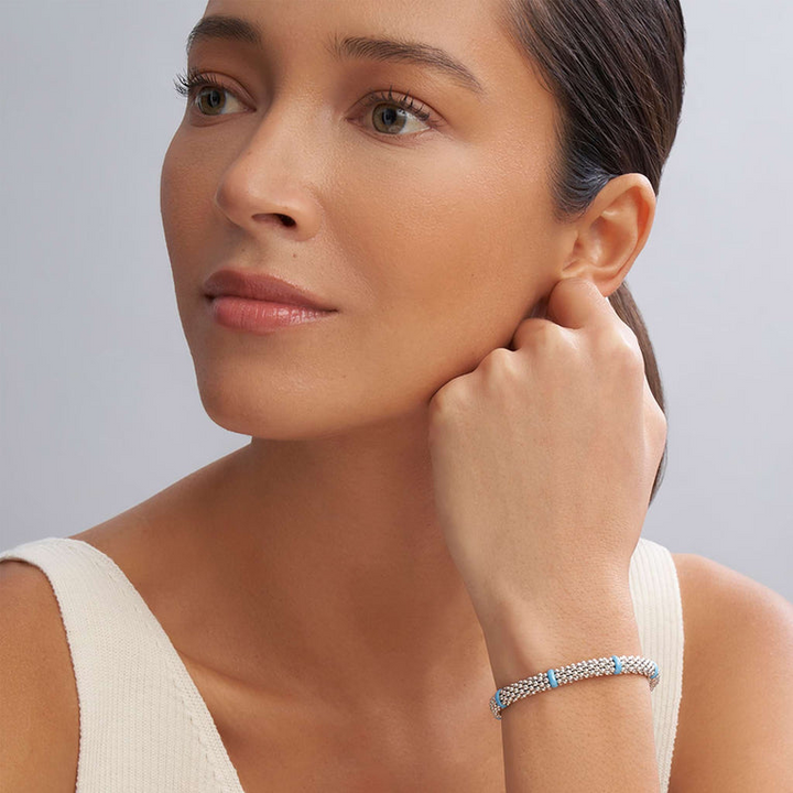 A woman is wearing a Sterling Silver & 18K Gold bracelet in the middle of a white background, featuring seven sterling silver stations and blue caviar beading