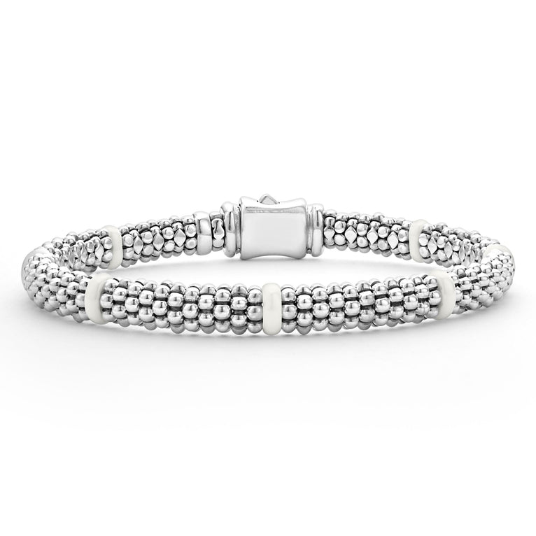 A close-up of a sterling silver and ceramic beaded bracelet in the middle of a white background featuring seven smooth white ceramic stations and silver Caviar beading.