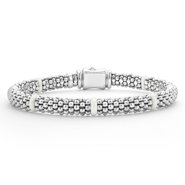 A close-up of a sterling silver and ceramic beaded bracelet in the middle of a white background featuring seven smooth white ceramic stations and silver Caviar beading.