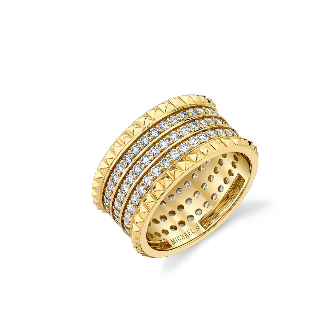 A yellow-gold ring lying flat against a white background. It features three rows of pave-set round diamonds between two bands of miniature pyramid studs.