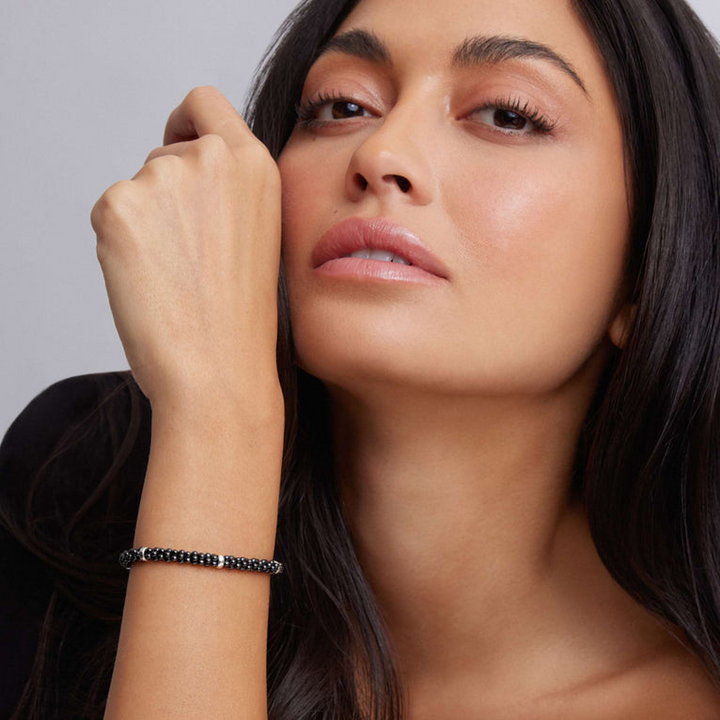 A woman wearing a Sterling silver and 18k gold bracelet featuring five sterling silver stations and black ceramic caviar beading.