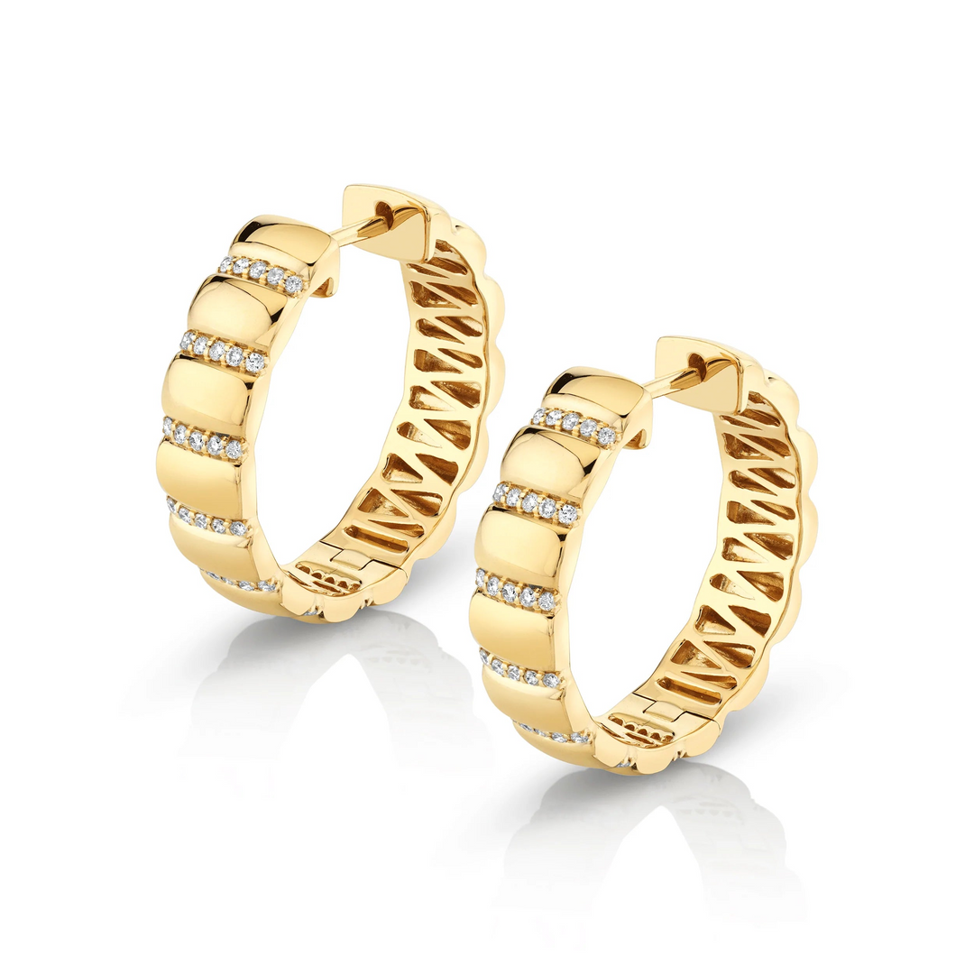 Two yellow-gold earrings are lying flat against a white background. The hoop earrings feature pave-set round diamond stations.