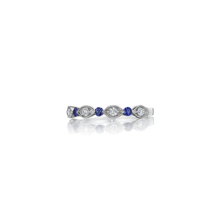 A white gold ring lies flat, showing the side of the ring against a white background. It features a diamond set band with marquise and sapphire detailing.