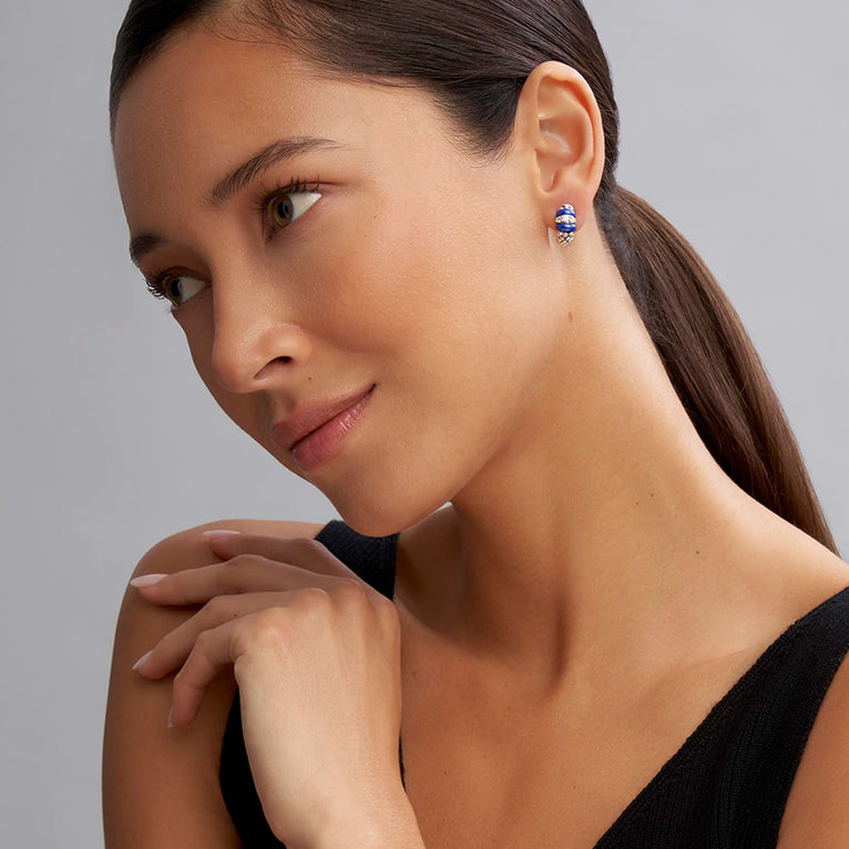 A close-up of a woman wearing a pair of huggie earrings with smooth ultramarine ceramic and diamonds with Caviar beading. 