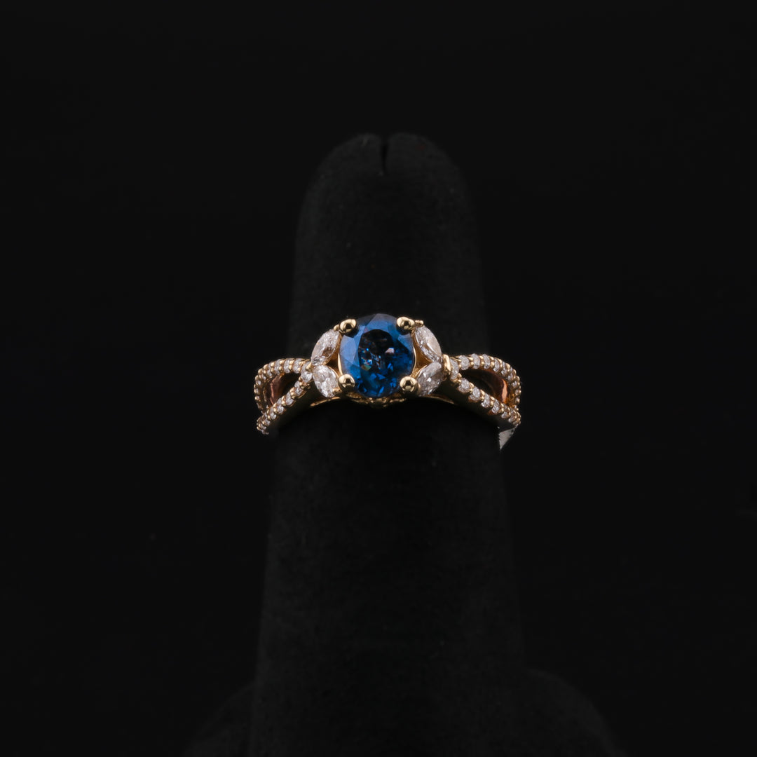 This is a close-up of a yellow-gold ring with a split shank. It showcases a brilliant center spinel elegantly held in place by four sparkling marquise diamonds. The ring rests on a black ring holder against a black background.