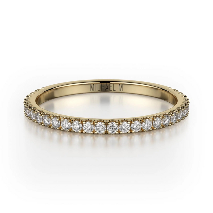 A yellow-gold ring lies flat against a white background. It features a bezel set of round diamonds, and the "Michael M" inscription is visible inside it.