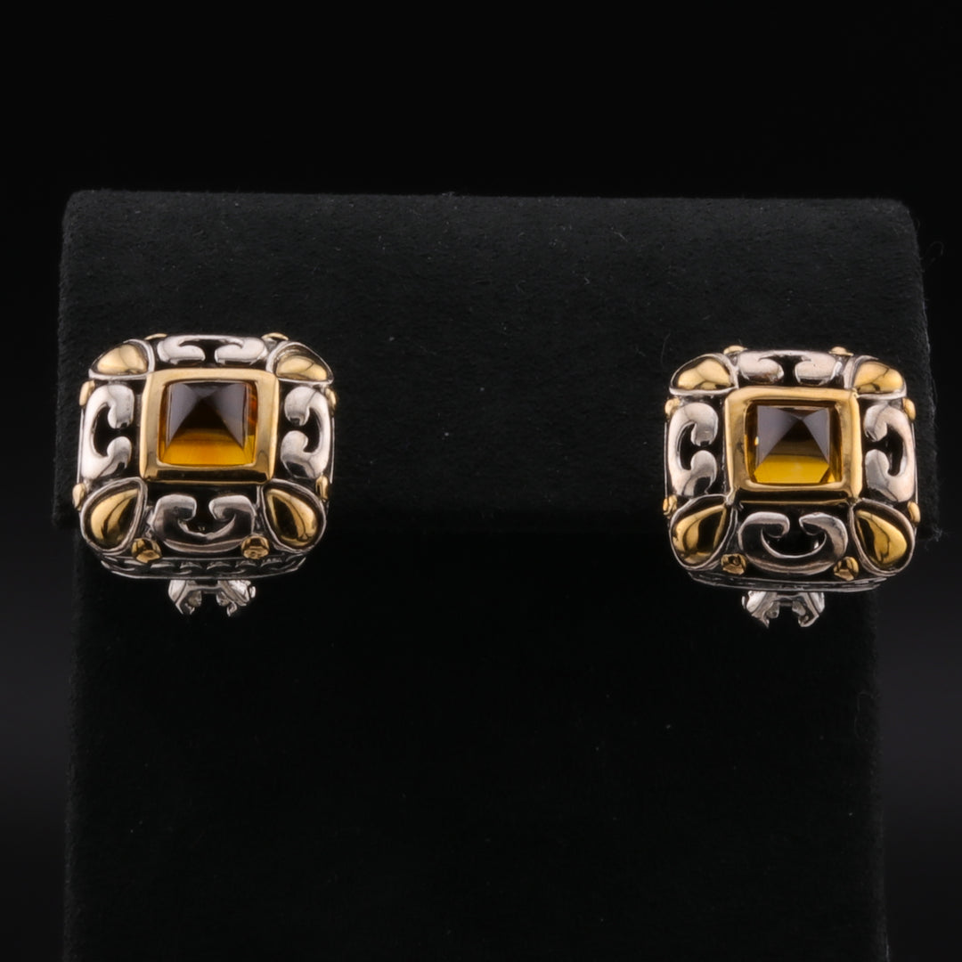 A pair of stud earrings with a smokey quartz gemstone set within a delicate filigree frame against a black background.