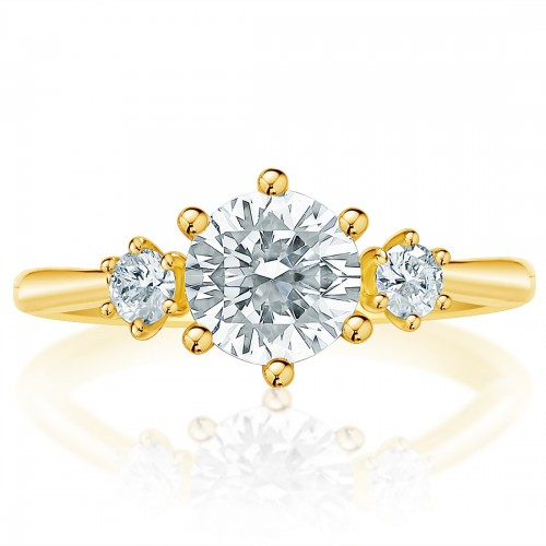 A ring made of yellow gold lies flat against a white background. It features a round-cut diamond set in the center with side stones.