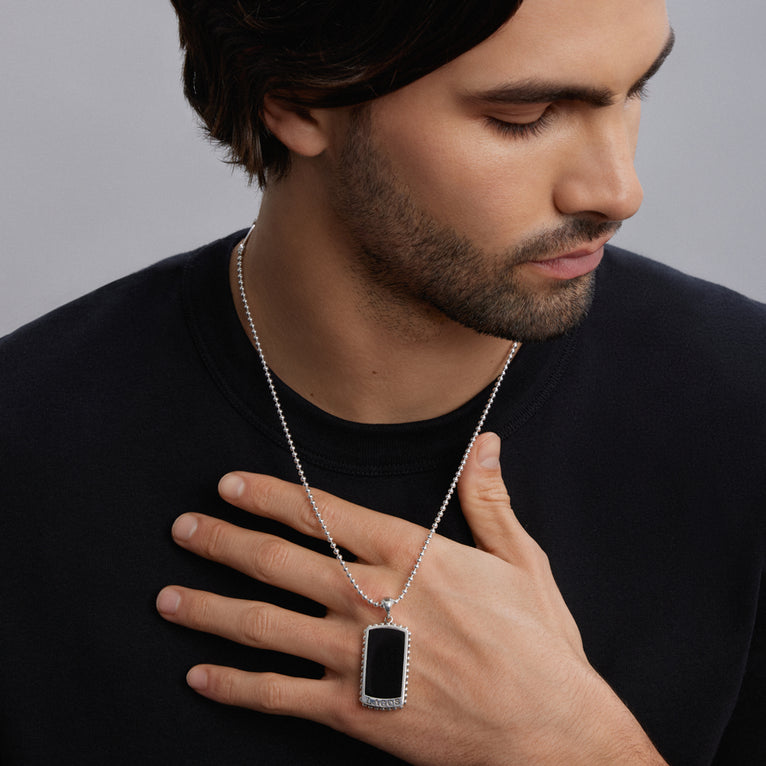 A man is wearing a tag amulet with a chain featuring Black agate accented by sterling silver Caviar beading