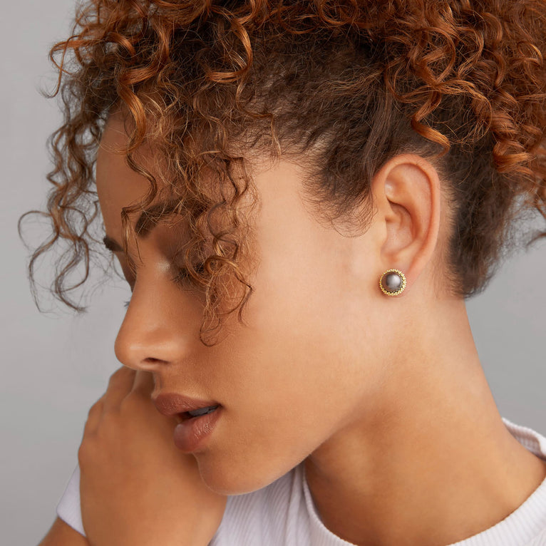 A woman wearing a white shirt and tahitian black pearl stud earrings set in 18K gold Caviar beading.