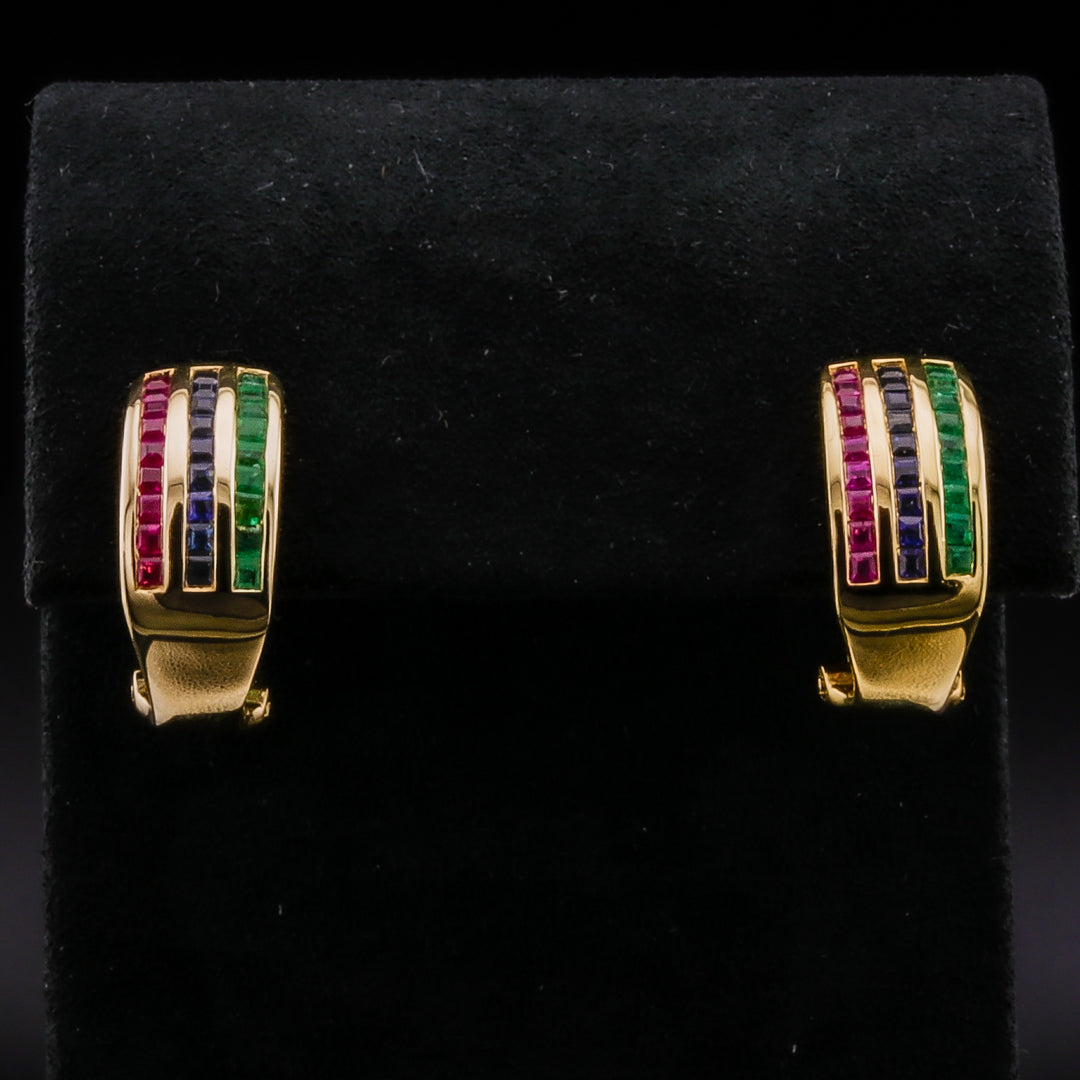 A pair of yellow-gold huggie earrings with a combination of rubies, emeralds, and sapphires, set in a yellow-gold lever back setting against a black background.