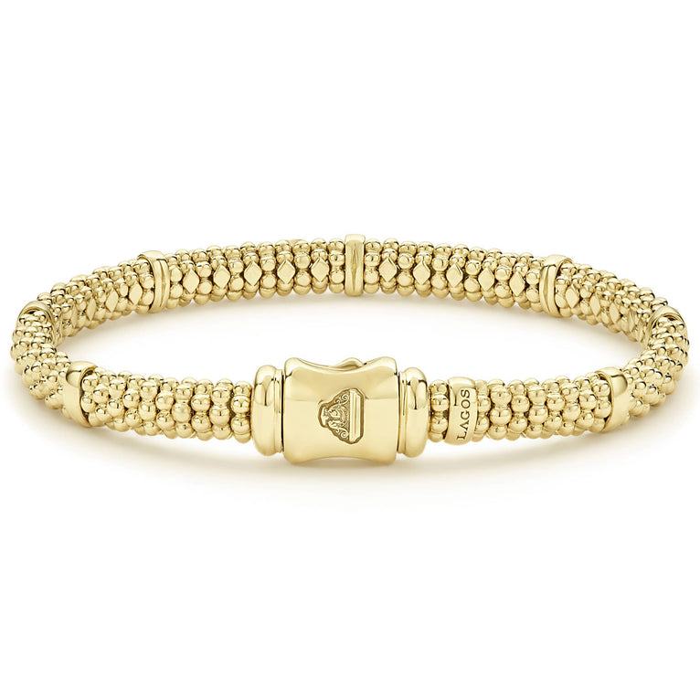 An 18k gold bracelet resting in the middle of a white background highlighting the gold clasp. The bracelet features smooth stations and caviar beading.