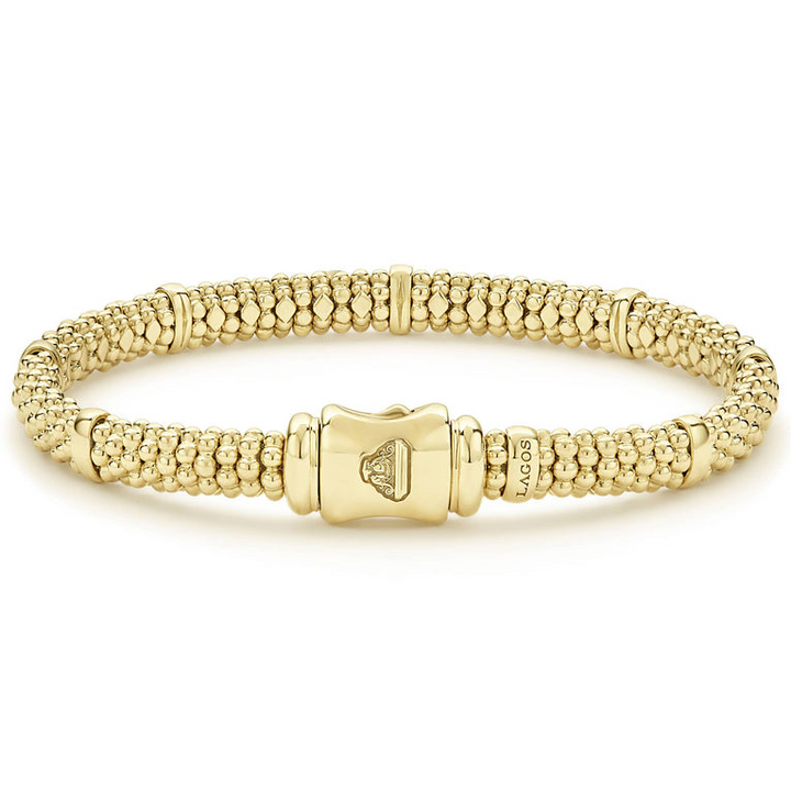 An 18k gold bracelet resting in the middle of a white background highlighting the gold clasp. The bracelet features smooth stations and caviar beading.