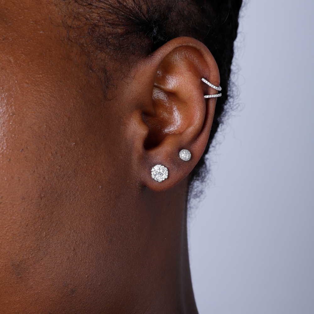 A woman with short black hair is wearing a pair of stud earrings with mixed-sized diamonds. 